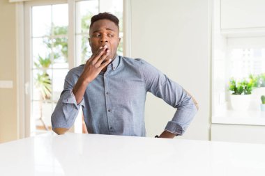 Beyaz masada yakışıklı afro-amerikan adam el ile ağız kapsayan yorgun esneme sıkılmış. Huzursuz ve uykululuk.