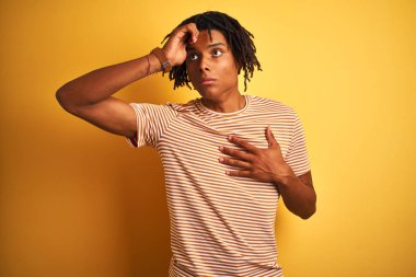 Hastalık ve ateş, grip ve soğuk algınlığı, virüs hasta için izole sarı arka plan dokunmadan alın üzerinde duran çizgili t-shirt giyen dreadlocks ile Afro adam