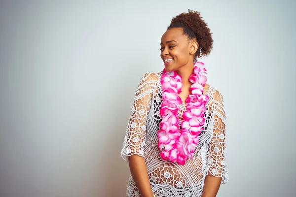 Young african american woman with afro hair wearing flower hawaiian lei over isolated background looking away to side with smile on face, natural expression. Laughing confident.
