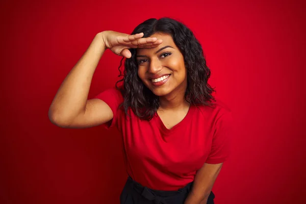 Beautiful transsexual transgender woman wearing t-shirt over isolated red background very happy and smiling looking far away with hand over head. Searching concept.