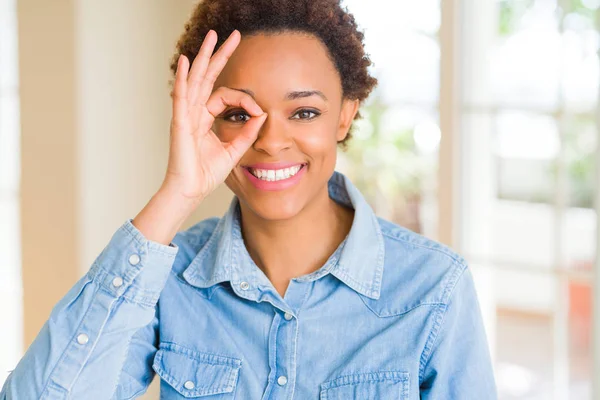 Young beautiful african american woman doing ok gesture with hand smiling, eye looking through fingers with happy face.
