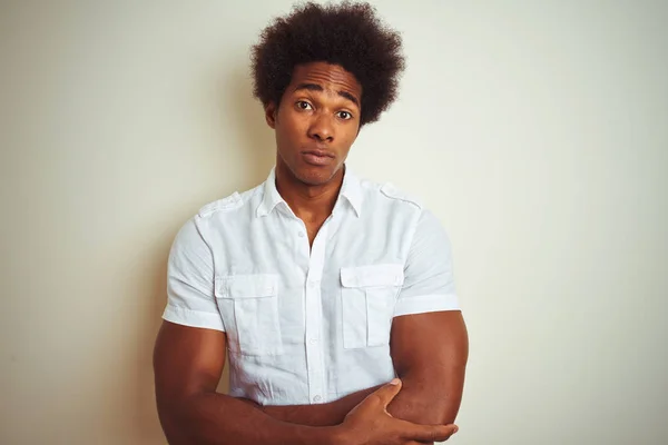 African american man with afro hair wearing shirt standing over isolated white background skeptic and nervous, disapproving expression on face with crossed arms. Negative person.