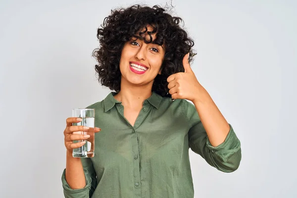 孤立した白い背景の上に水のガラスを保持する巻き毛を持つ若いアラブの女性は Okサインをやって大きな笑顔で幸せ 指で親指 優れた兆候 — ストック写真