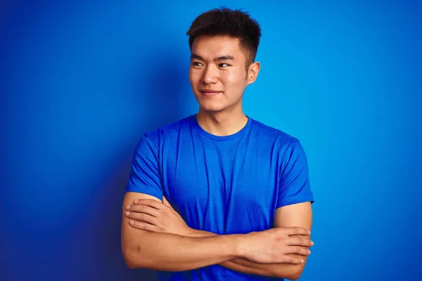 孤立した青い背景の上に立つTシャツを着たアジアの若い中国人男性が横を見つめ 考え方を見つめている — ストック写真