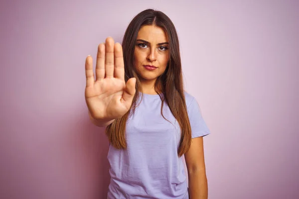 Young beautiful woman wearing casual t-shirt standing over isolated pink background doing stop sing with palm of the hand. Warning expression with negative and serious gesture on the face.
