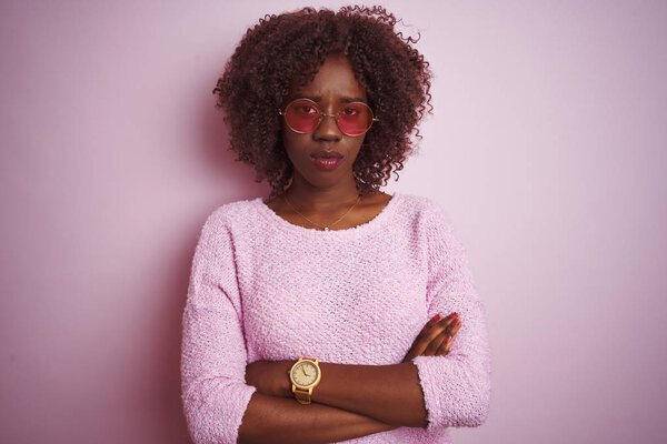 Young african afro woman wearing sweater and sunglasses over isolated pink background skeptic and nervous, disapproving expression on face with crossed arms. Negative person.