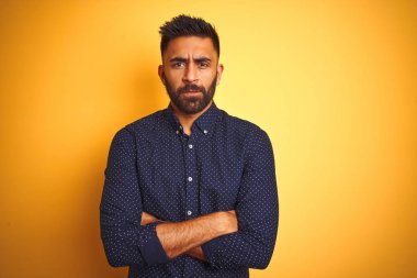 Genç yakışıklı Hintli işadamı izole sarı arka plan üzerinde gömlek giyen şüpheci ve sinirli, çapraz kolları ile yüzünde onaylamayan ifade. Negatif kişi.