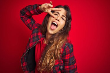 Genç güzel kadın kırmızı izole arka plan üzerinde duran rahat ceket giyen el hareketi ile sembolik silah holding, çekim silah öldürme oynarken, öfkeli yüz