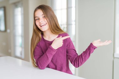 Beyaz masada güzel genç kız çocuk hayran ve el ile sunmak ve parmak ile işaret ederken kameraya gülümsüyor.
