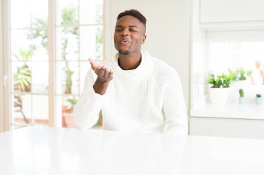 Beyaz masada yakışıklı Afrikalı Amerikalı adam güzel ve seksi olmak hava el ile bir öpücük üfleme kamera bakıyor. Aşk ifadesi.