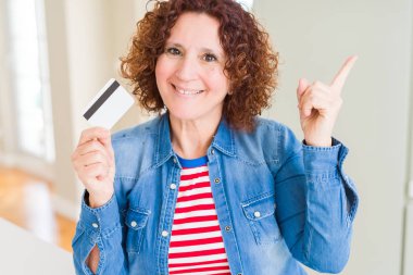 Ödeme olarak kredi kartı tutan kıdemli kadın çok mutlu yan el ve parmak ile işaret