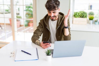 Akıllı telefon kullanarak ve dizüstü bilgisayar kullanarak eğitim genç öğrenci adam çok mutlu ve heyecanlı, kazanan ifade büyük bir gülümseme ile çığlık zafer kutluyor ve ellerini kaldırdı