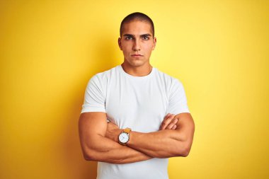 Genç beyaz adam sarı izole arka plan üzerinde rahat beyaz t-shirt giyen şüpheci ve sinirli, çapraz kolları ile yüzünde onaylamayan ifade. Negatif kişi.