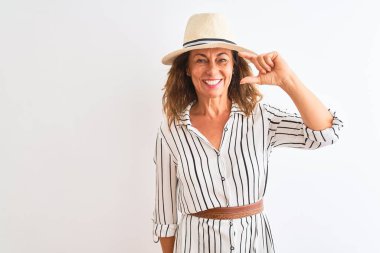 Izole beyaz arka plan üzerinde çizgili elbise ve şapka giyen orta yaş iş kadını gülümseyerek ve el parmakları görünümlü ve kamera ile küçük boyutlu işareti yapıyor emin gesturing. Ölçü kavramı.