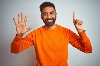 Genç hintli adam izole beyaz arka plan üzerinde turuncu kazak giyen gösteren ve parmakları ile işaret ederken emin ve mutlu gülümseyerek altı numara.