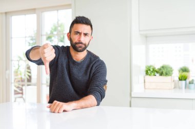 Yakışıklı İspanyol adam evde rahat kazak giyen mutsuz ve kızgın gösteren reddi gösteren ve başparmak aşağı jest ile negatif. Kötü ifade.