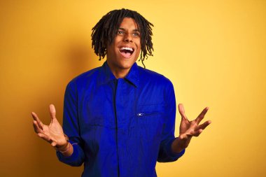 Izole sarı arka plan üzerinde mekanik üniforma giyen dreadlocks ile Afro işçi adam deli ve deli bağırarak ve agresif ifade ve kollar kaldırdı ile bağırıyor. Hayal kırıklığı kavramı.