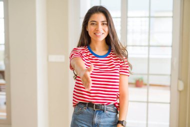 Tebrik ve konuksever dost sunan karşılıklı gülümseyen rahat t-shirt giyen genç güzel kadın. Başarılı iş.