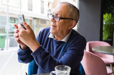Mutlu ve zevk rahatlatıcı smartphone kullanarak emeklilik gülümseyen restaurante, kahve içme yakışıklı orta yaş komuta sizde