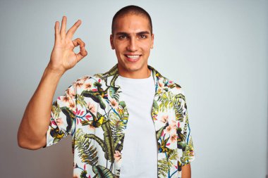 Genç yakışıklı adam tatilbeyaz arka plan üzerinde Hawaii gömlek giyen olumlu el ve parmaklar ile ok işareti yapıyor gülümseyerek. Başarılı ifade.