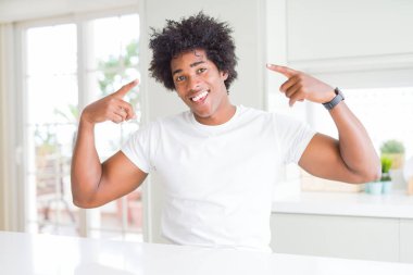 Genç afro-amerikan adam rahat beyaz t-shirt giyen evde gülümseyerek iki eliyle parmak, harika bir fikir ya da düşünce, iyi bellek ile baş işaret