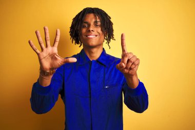 Afro işçi adam dreadlocks izole sarı arka plan üzerinde mekanik üniforma giyen gösteren ve parmakları ile işaret ederken emin ve mutlu gülümseyerek altı numara.