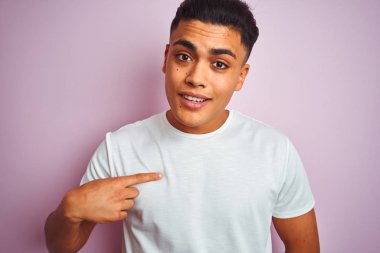 Kendine işaret eden sürpriz yüzü ile izole pembe arka plan üzerinde duran t-shirt giyen genç Brezilyalı adam