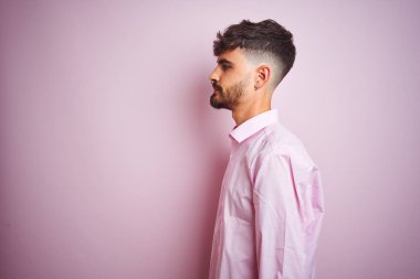 Yan bakan izole pembe arka plan üzerinde duran gömlek giyen dövme giyen genç adam, kendine güvenen gülümseme ile doğal yüz ile profil poz dinlenmek.