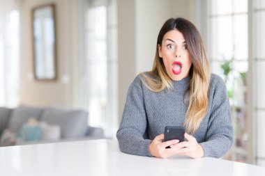 Evde akıllı telefonu kullanan genç güzel kadın sürpriz bir yüzle şokta korkmuş, korku ve korku yla heyecanlı ifade