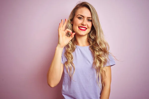 분홍색 서있는 보라색 티셔츠를 아름다운 여성은 손가락으로 기호를하고 긍정적 미소를 — 스톡 사진