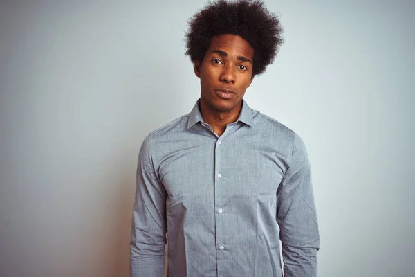 Young african american man with afro hair wearing grey shirt over isolated white background with serious expression on face. Simple and natural looking at the camera.