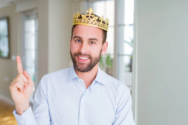 英俊的商人戴着金色的皇冠作为国王或王子 脸上带着灿烂的笑容 用手和手指指着一边看着相机 — 图库照片