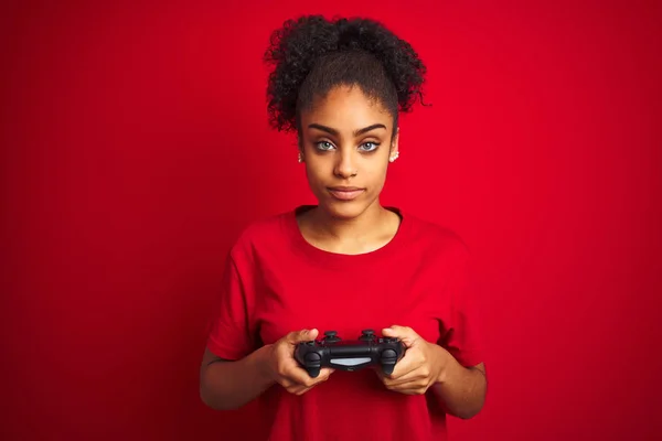 非洲裔美国玩家妇女玩视频游戏使用操纵杆在孤立的红色背景与智能脸的自信表情思考认真 — 图库照片