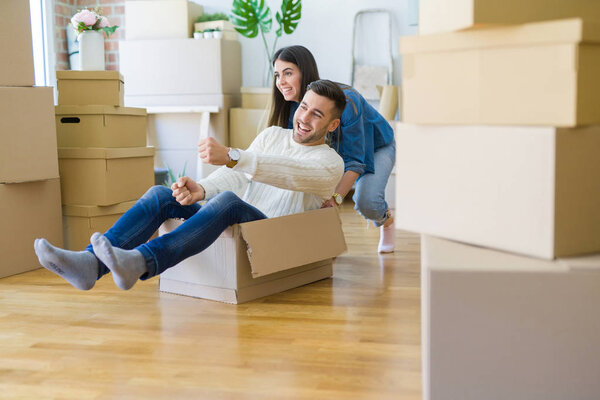 Young couple moving to a new home, having fun riding cardboard boxes