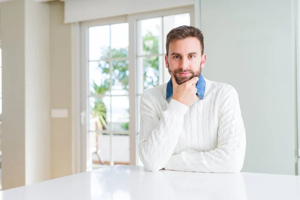 Handsome man wearing casual sweater looking confident at the camera with smile with crossed arms and hand raised on chin. Thinking positive.