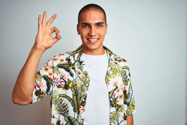 休日の若いハンサムな男は 白い背景の上にハワイのシャツを着て 手と指でOkサインをやって肯定的に微笑んでいます 成功した式 — ストック写真