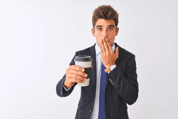 Young handsome businessman wearing suit holding coffee over isolated white background cover mouth with hand shocked with shame for mistake, expression of fear, scared in silence, secret concept