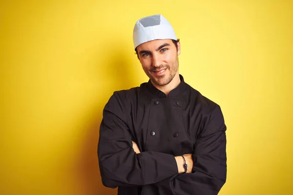 年轻的英俊厨师男子做饭穿着制服和帽子在孤立的黄色背景快乐的脸微笑与交叉的手臂看着相机 积极的人 — 图库照片