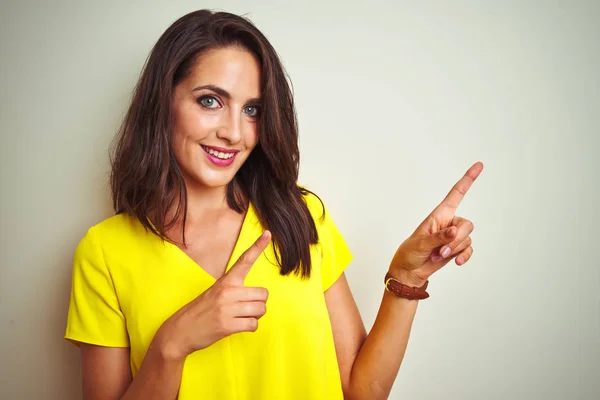年轻的漂亮女人穿着黄色T恤站在白色孤立的背景微笑 看着相机指着两只手和手指的一侧 — 图库照片