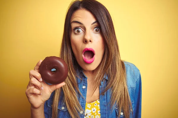 年轻的美女吃巧克力甜甜圈在黄色的背景害怕在震惊与惊喜的脸 害怕和兴奋与恐惧的表情 — 图库照片