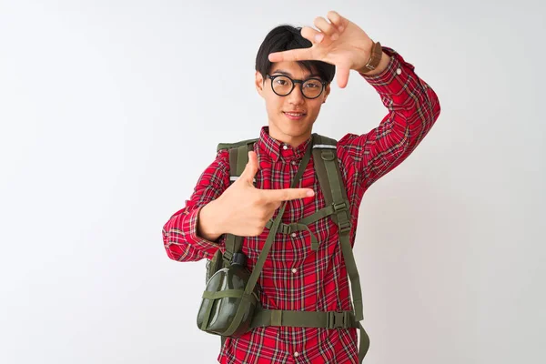 Chinese hiker man wearing backpack canteen glasses over isolated white background smiling making frame with hands and fingers with happy face. Creativity and photography concept.