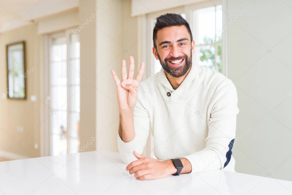 Handsome hispanic man wearing casual white sweater at home showing and pointing up with fingers number four while smiling confident and happy.