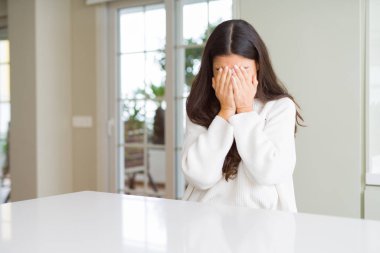 Ağlarken elleri ile yüz kapsayan üzücü ifade ile beyaz masada evde genç güzel kadın. Depresyon konsepti.