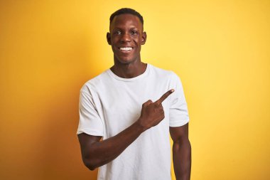 Beyaz t-shirt giyen genç afro-amerikan adam izole sarı arka plan neşeli bir yüz yüzü ile işaret eden bir gülümseme ile neşeli yüzünde mutlu ve doğal ifade ile yan yana