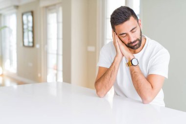 Yakışıklı İspanyol adam evde rahat beyaz t-shirt uyku yorgun rüya ve kapalı gözlerle gülümseyerek birlikte elleri ile poz.