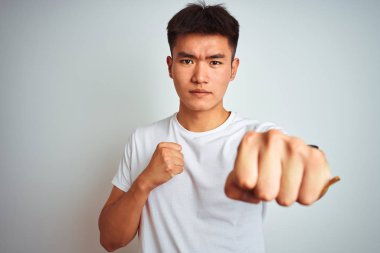 Genç Asyalı Çinli adam izole beyaz arka plan yumruk yumruk üzerinde duran t-shirt giyen mücadele, agresif ve öfkeli saldırı, tehdit ve şiddet