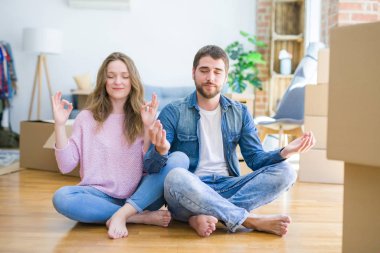 Genç güzel çift katta oturan yeni bir eve hareket ve gözleri parmakları ile meditasyon jest yapıyor kapalı gülümseyerek. Yoga konsepti.