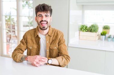 Beyaz masanın üzerinde oturan rahat ceket giyen genç adam komik ifade ile mutlu dil dışarı yapışmasını. Duygu kavramı.