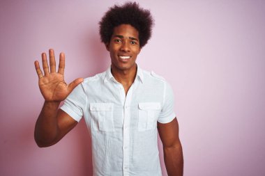 Afro saçlı beyaz gömlek giyen genç amerikalı adam izole pembe arka plan üzerinde duran gösteren ve parmakları ile işaret ederken emin ve mutlu gülümseyerek beş.