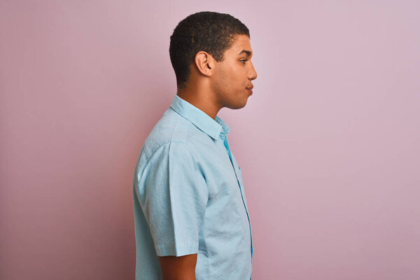 Young handsome arab man wearing blue shirt standing over isolated pink background looking to side, relax profile pose with natural face with confident smile.